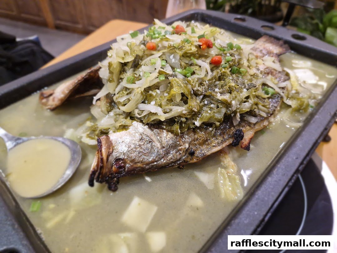 A close-up shot of a claypot dish featuring a whole fish topped with pickled vegetables and chili.