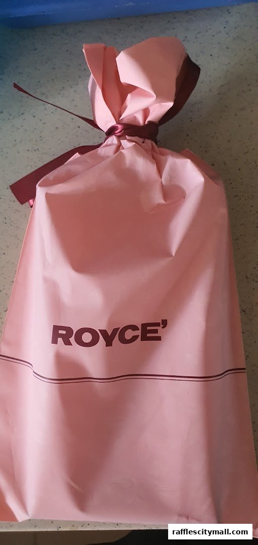 A pink gift bag with the Royce logo and a burgundy ribbon tie.