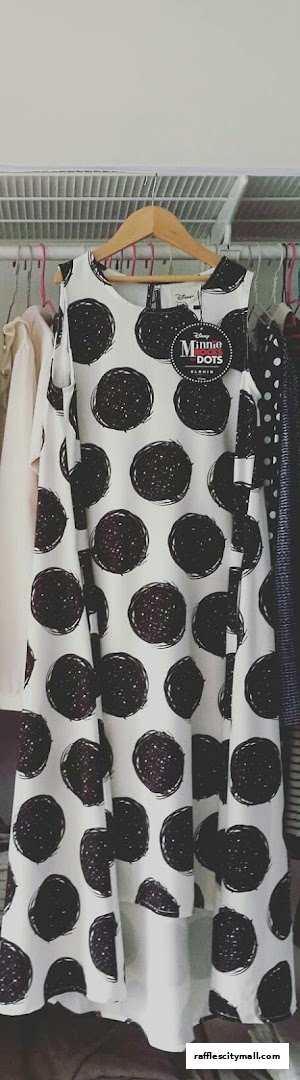 A white dress with black polka dots hanging on a hanger in a closet.