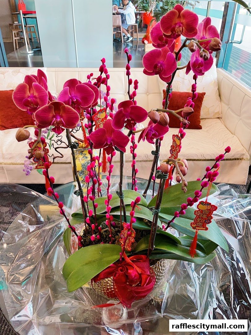 A vibrant arrangement of pink orchids and pussy willow branches with festive red decorations.