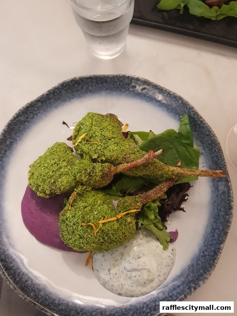 A plate of lamb chops coated in green seasoning, served with mashed purple sweet potato and a side of sauce.