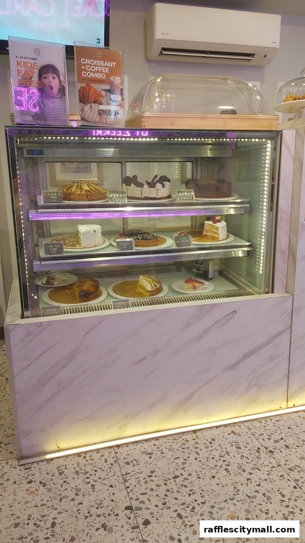 A display case filled with various cakes and pastries, with promotional posters above.