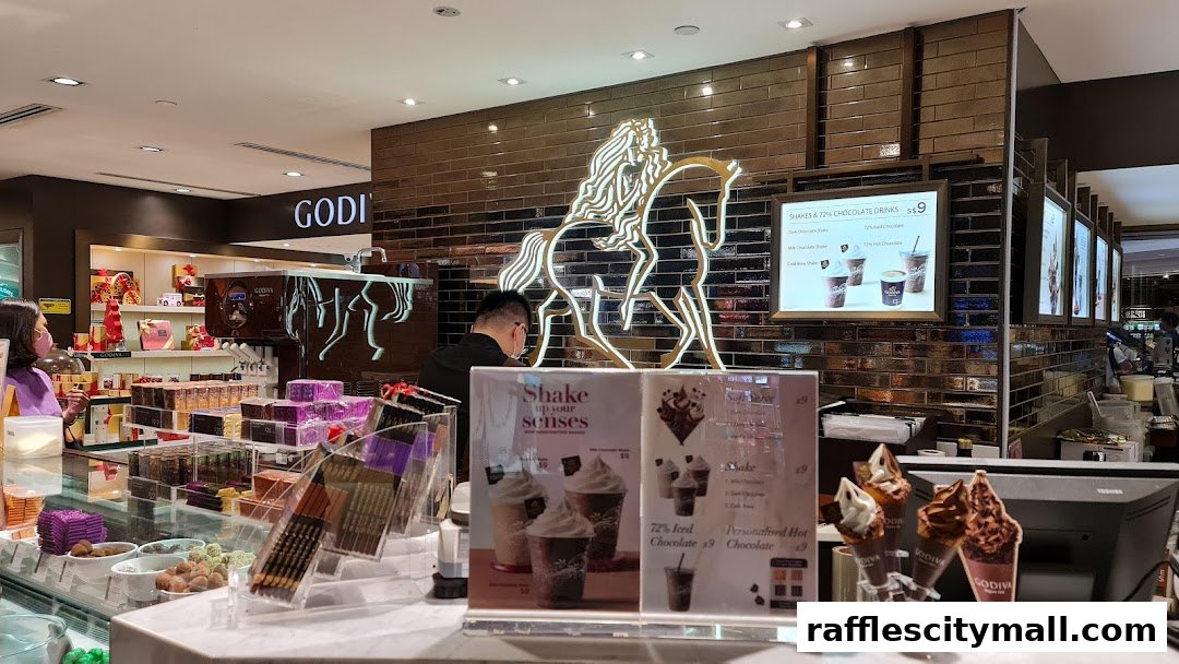 Interior of a Godiva chocolate shop with displays of chocolates and a counter with drinks and ice cream.