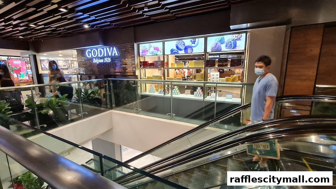 The Godiva chocolate shop entrance with illuminated displays and people on escalators.