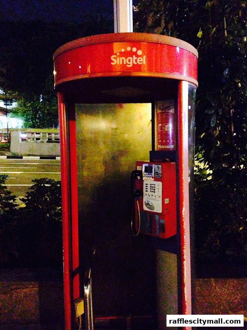 A red Singtel public payphone booth with a phone and keypad visible.