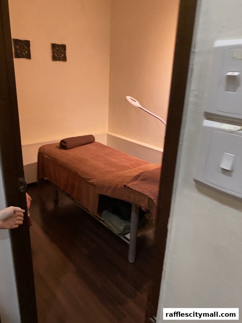 A treatment room with a massage bed, lamp, and decorative wall hangings.