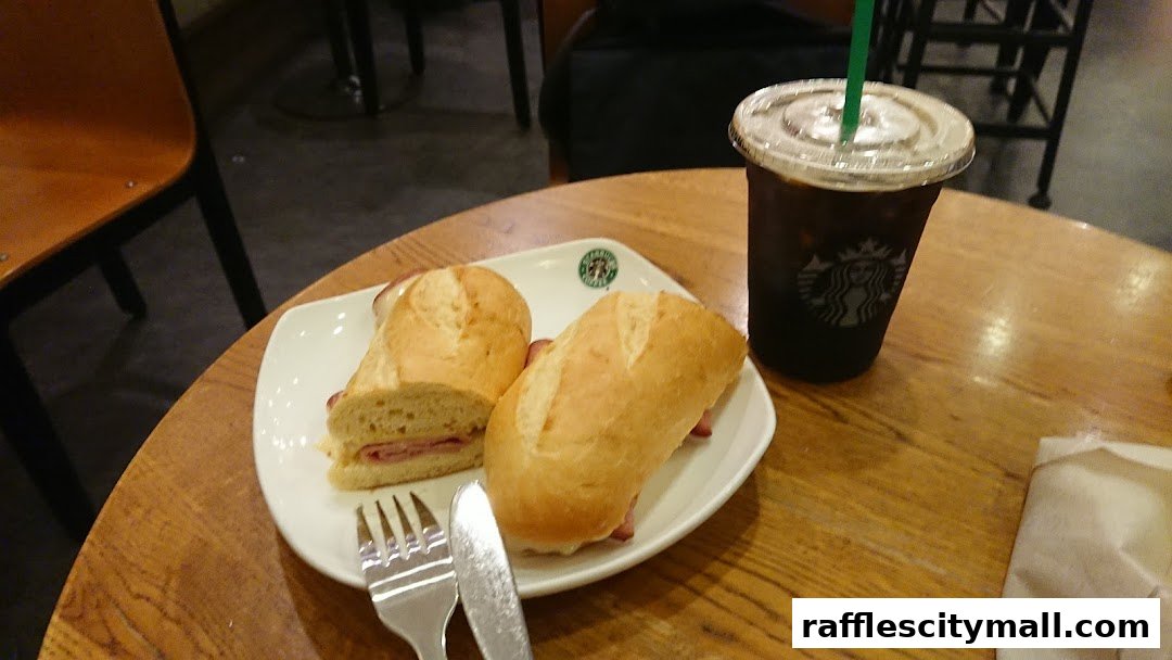 A Starbucks coffee and a sandwich served on a white plate with cutlery on a wooden table.