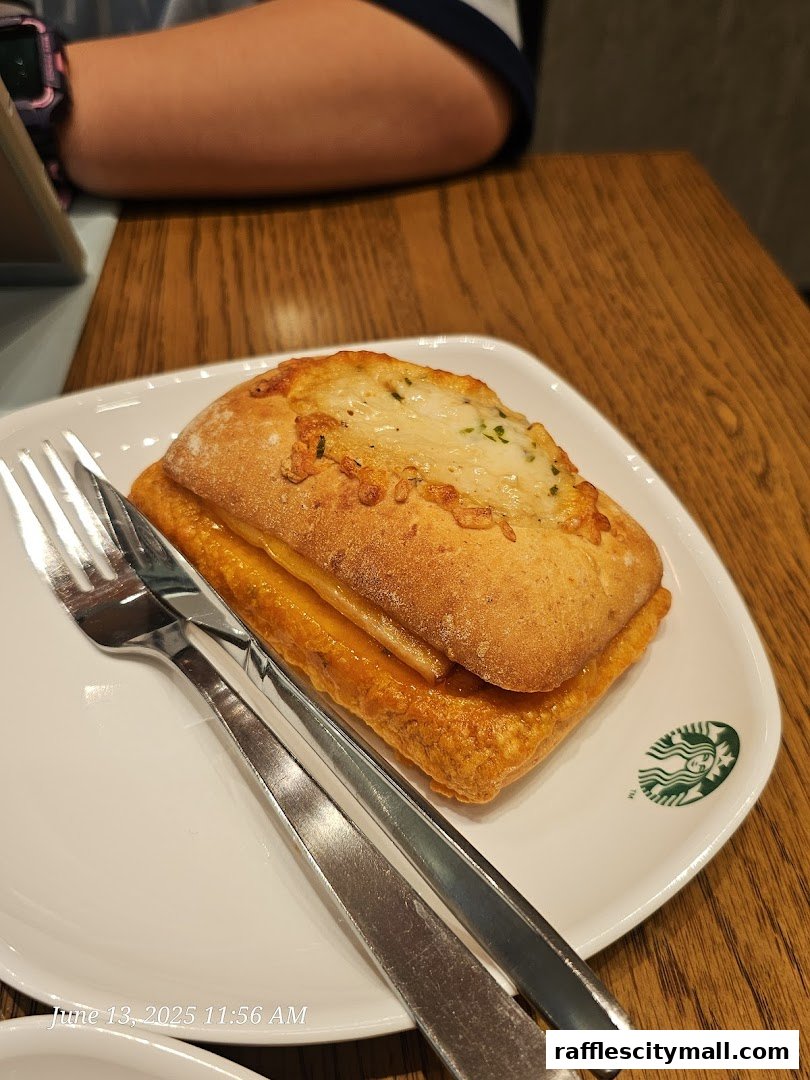 A close-up of a sandwich with cheese and a fork and knife on a Starbucks plate.