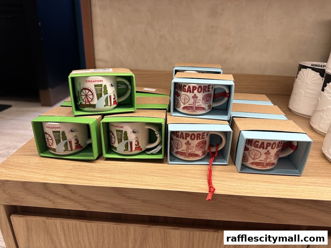 Several small mugs with Singapore landmarks are displayed in their boxes on a wooden counter.