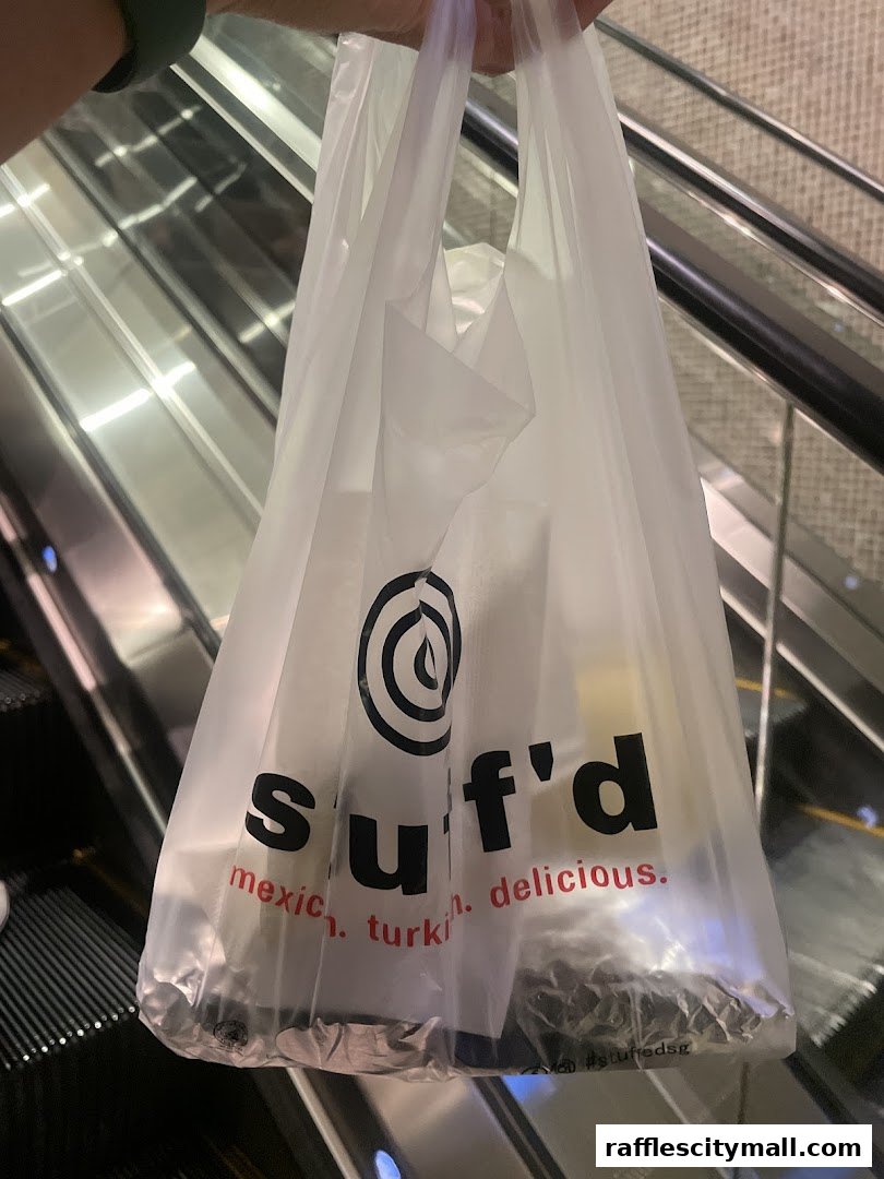 A person holds a Stuff'd plastic bag with food inside, in front of an escalator.