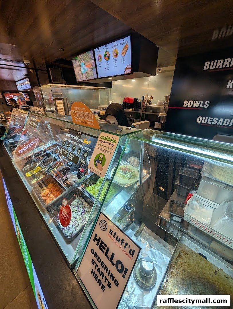 A food counter with various ingredients displayed, a menu board, and staff preparing food.