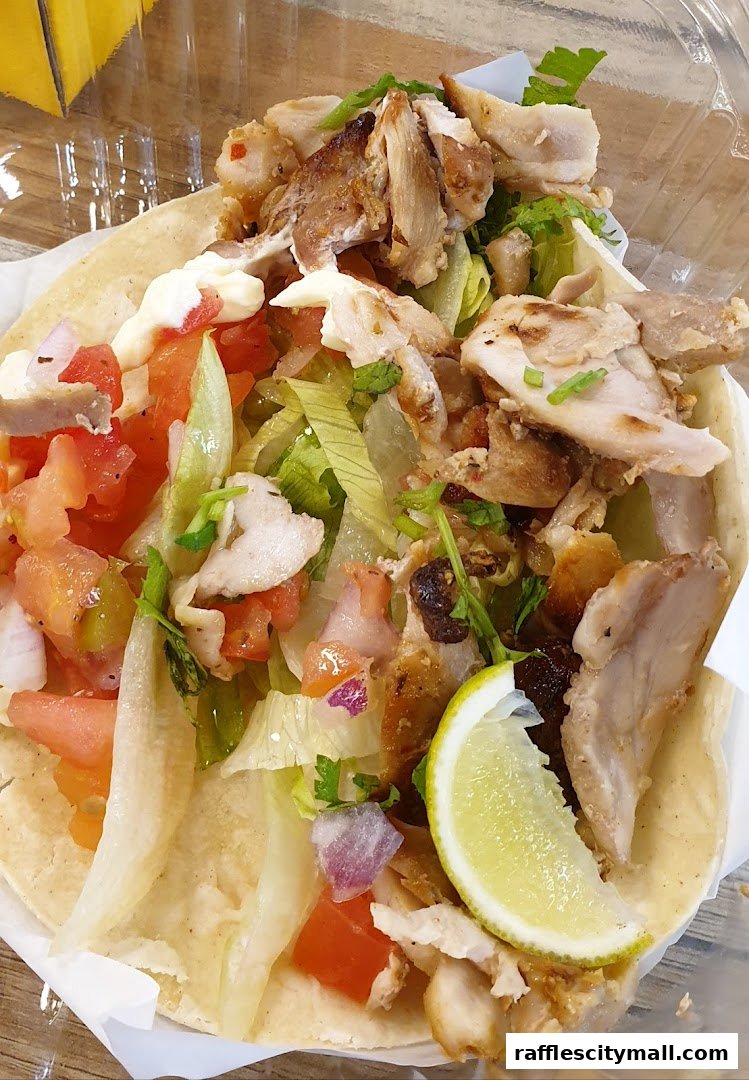 A close-up of a delicious chicken taco with fresh toppings and a lime wedge.