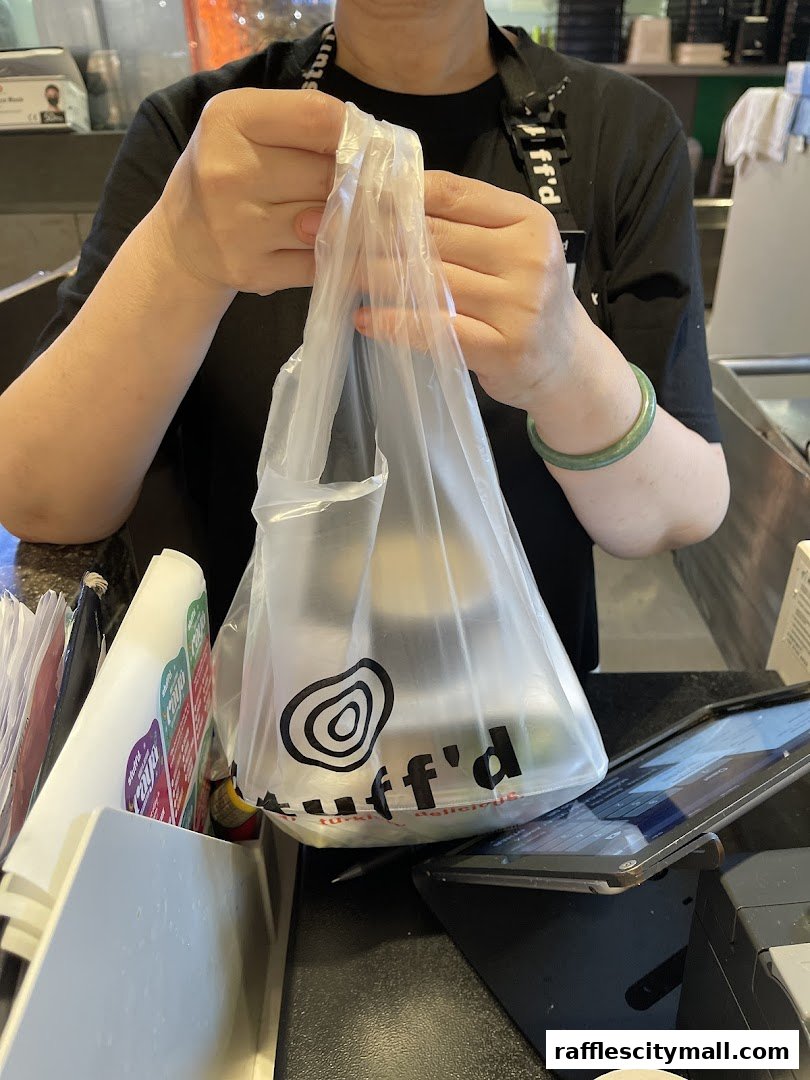 A person holds a Stuffd branded plastic bag filled with food items.