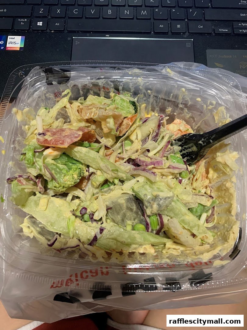 A close-up of a fresh salad in a clear plastic container with a fork.