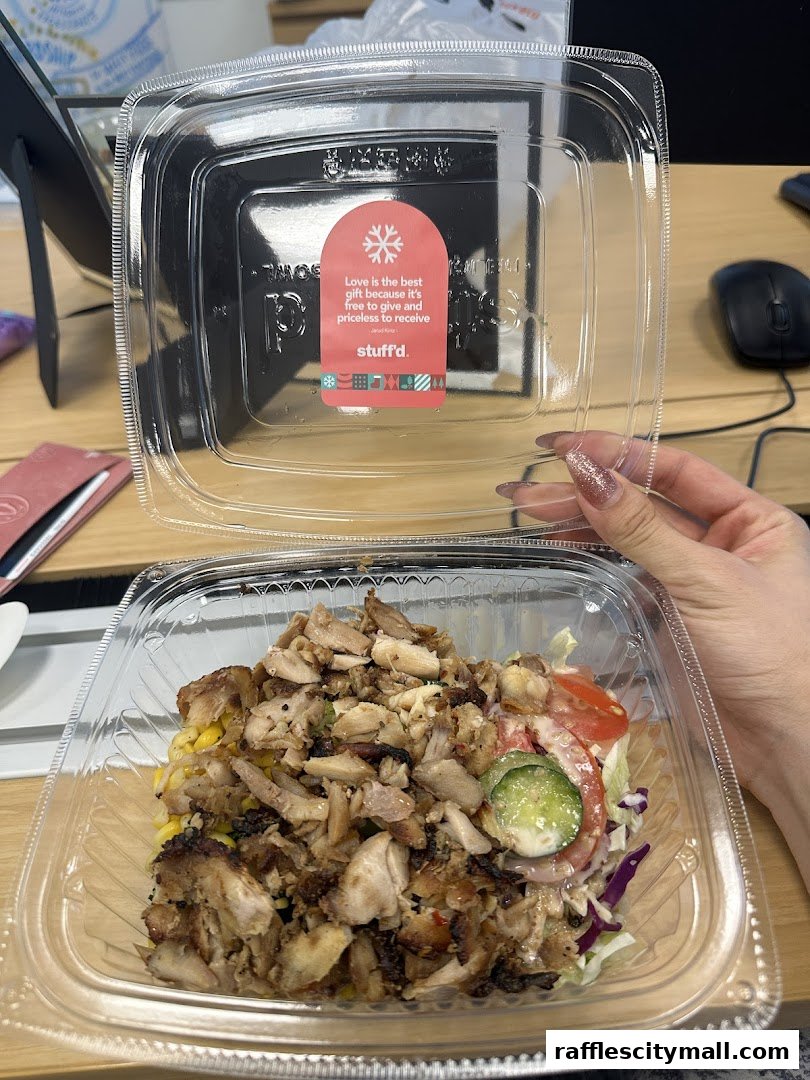 A person holds a clear plastic container filled with a chicken salad and vegetables.