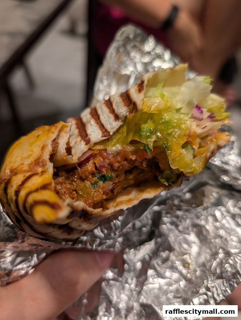 A close-up shot of a delicious wrap filled with meat, lettuce, and sauce, held in foil.
