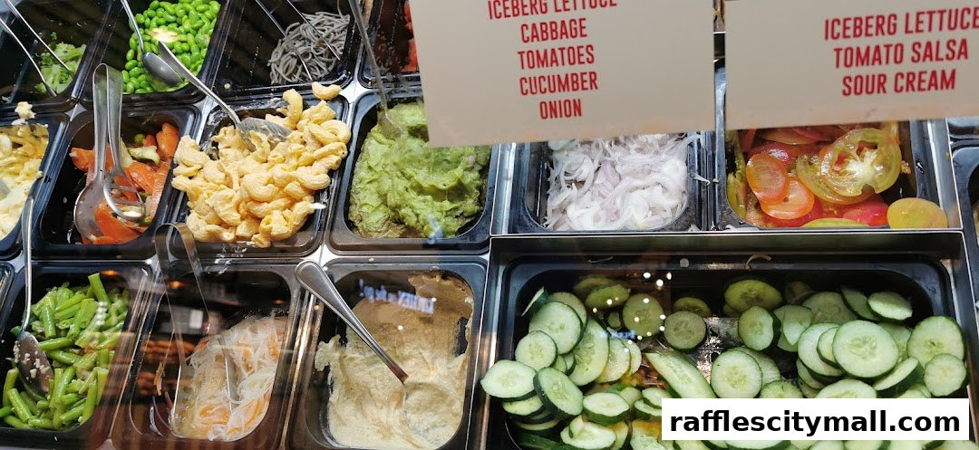 A display of fresh ingredients for salads and bowls, including pasta salad, guacamole, and sliced cucumbers.