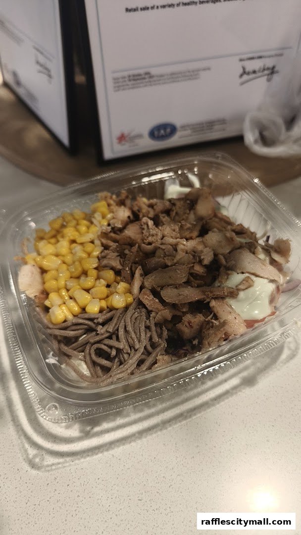 A clear plastic container filled with a meal featuring meat, corn, and noodles.