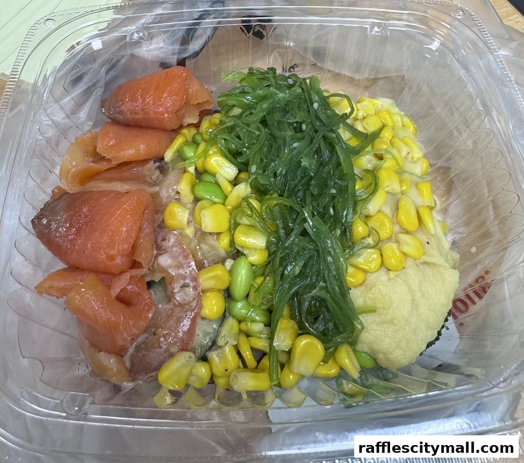 A clear plastic container filled with a colorful poke bowl featuring salmon, corn, edamame, and seaweed salad.