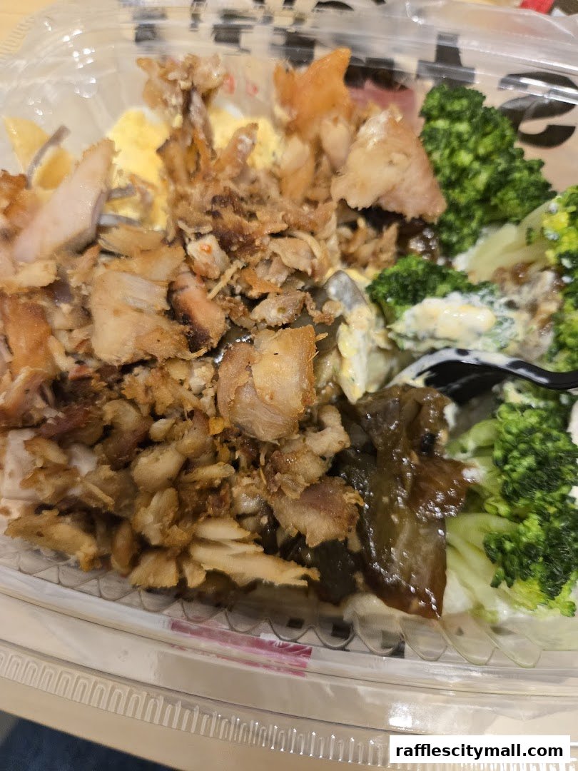 A close-up of a takeout container filled with rice, seasoned meats, broccoli, and other toppings.