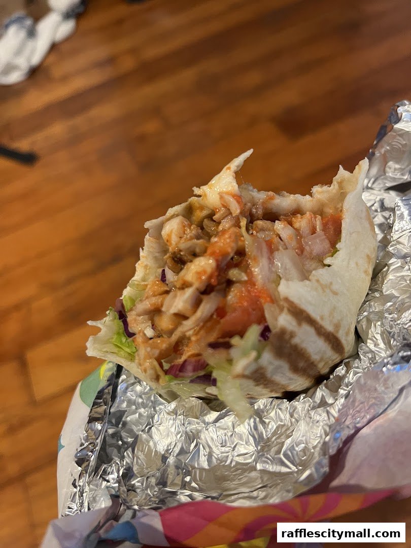 A close-up of a delicious wrap filled with meat, vegetables, and sauce, wrapped in foil.