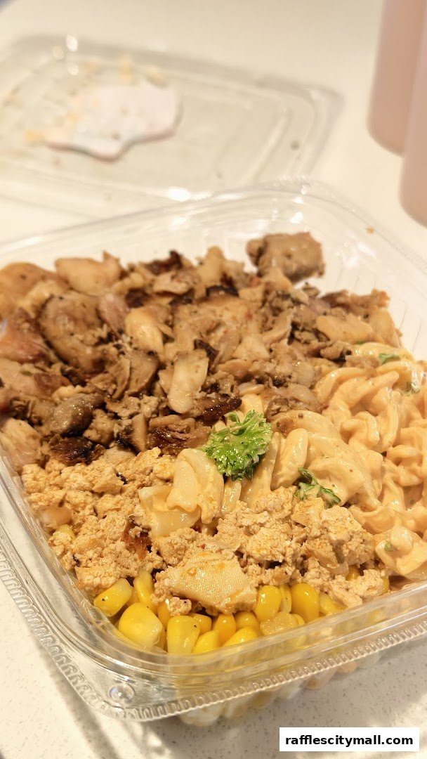 A clear plastic container filled with a colorful and diverse meal, featuring meat, pasta, and corn.