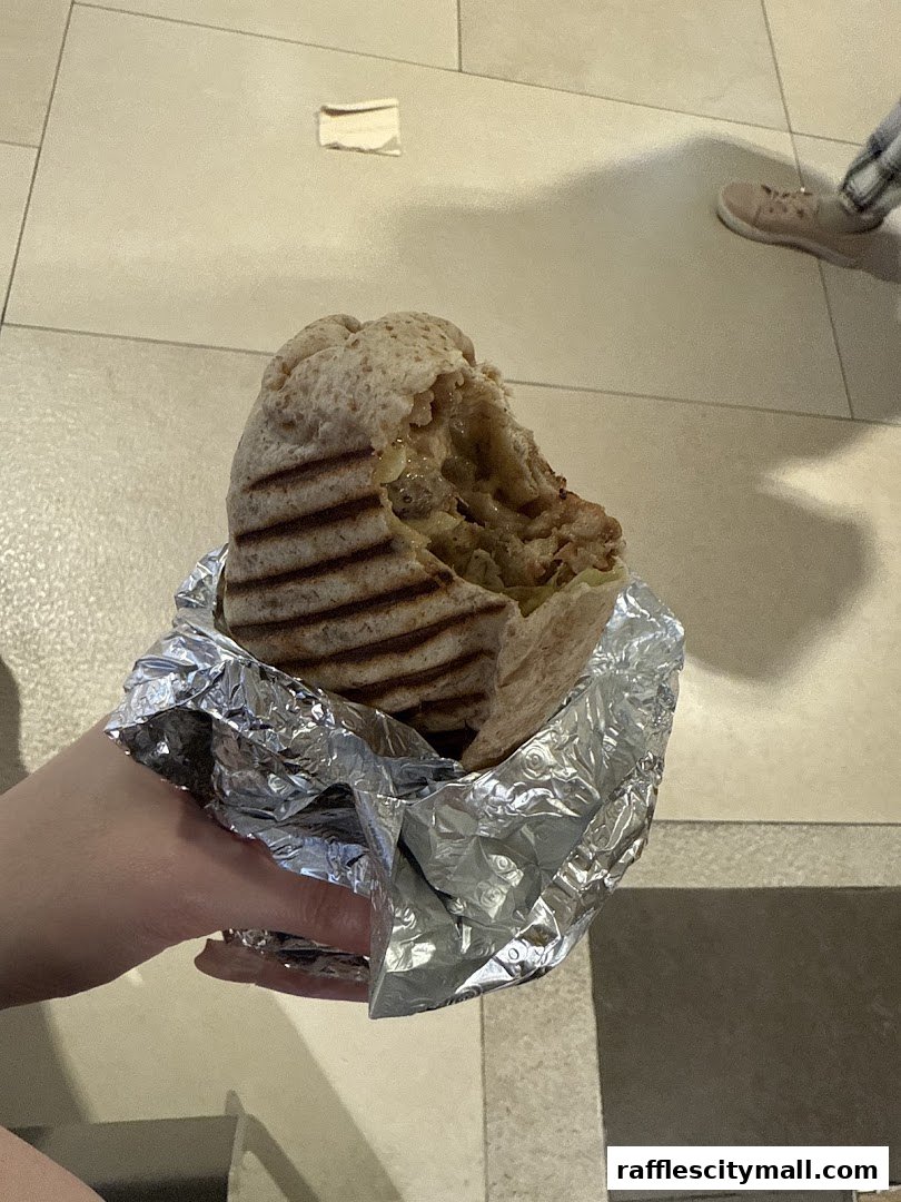 A hand holds a partially eaten grilled sandwich wrapped in foil.