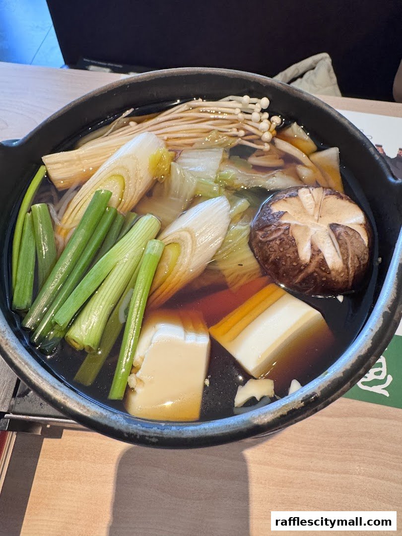 A close-up of a hot pot dish with tofu, mushrooms, leeks, and enoki mushrooms in broth.