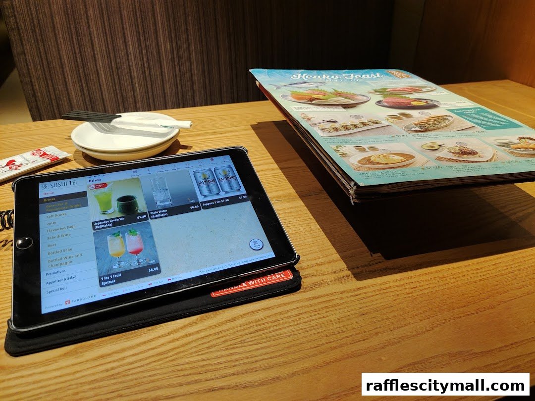 A tablet displaying a digital menu and a physical menu on a wooden table at Sushi Tei.