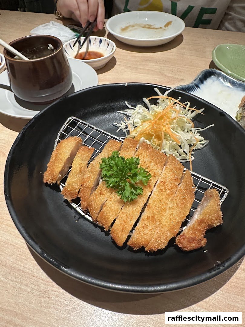 A plate of crispy fried pork cutlet with shredded cabbage and a dipping sauce.