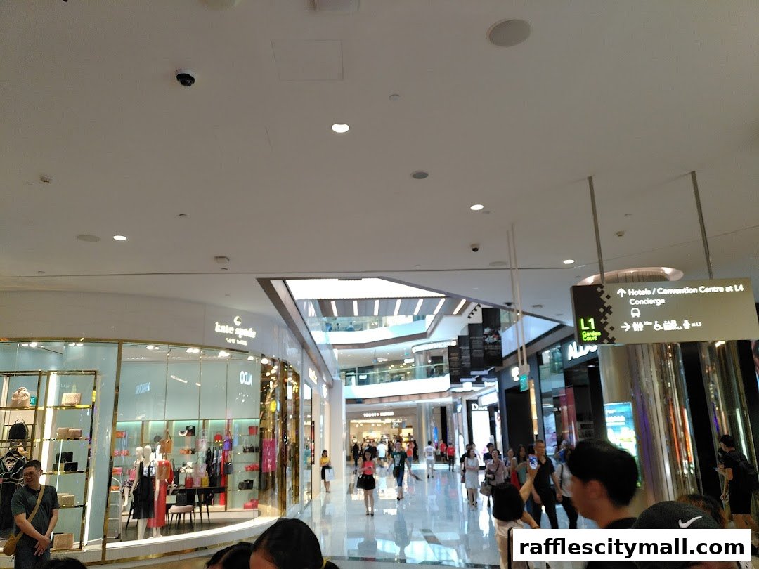A busy shopping mall interior with various shops and shoppers walking around.