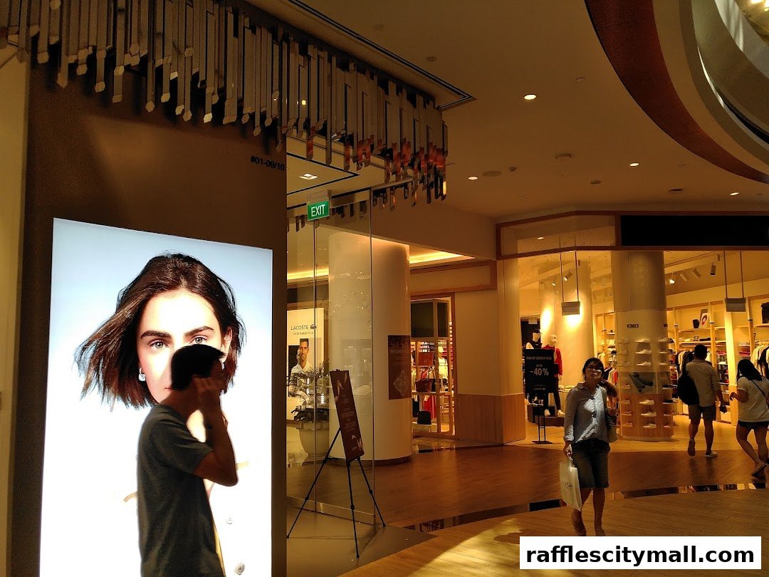 People walking past a brightly lit display and a retail store in a shopping mall.