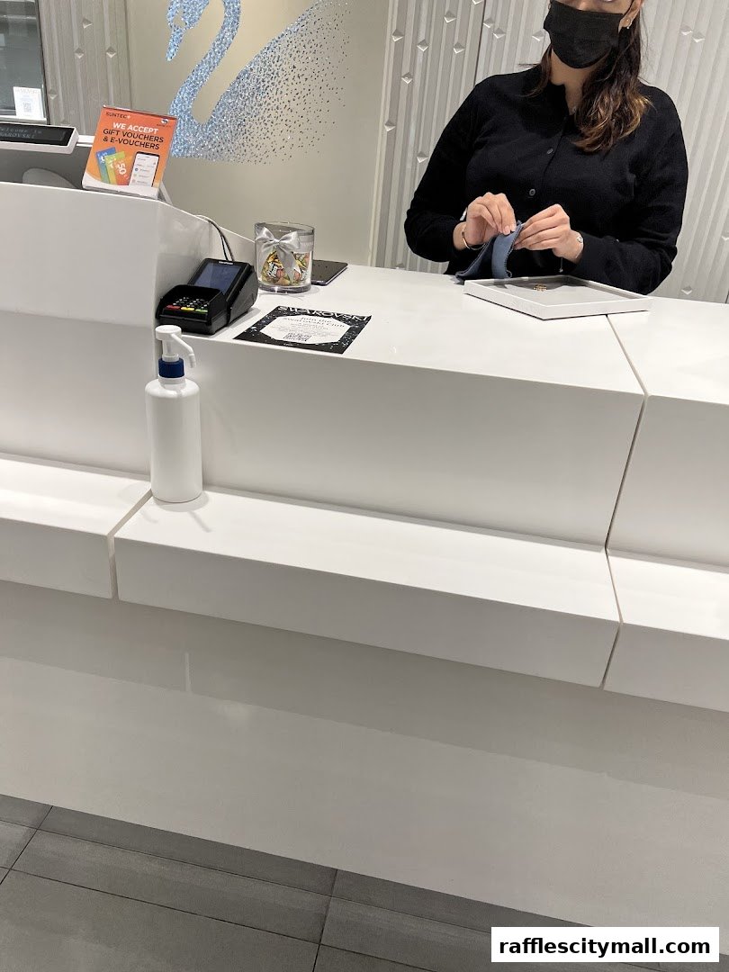 A store employee at the counter of a Swarovski store, with a hand sanitizer and payment terminal visible.