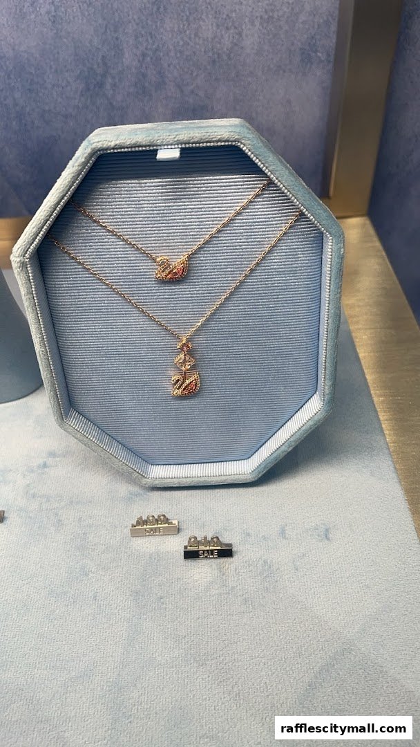 Two swan necklaces displayed in a blue velvet jewelry box, with 'SALE' signs in the foreground.