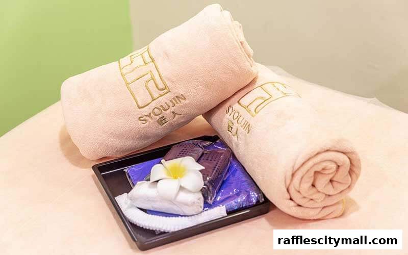 Two rolled towels with the Syoujin logo and a tray of spa accessories.