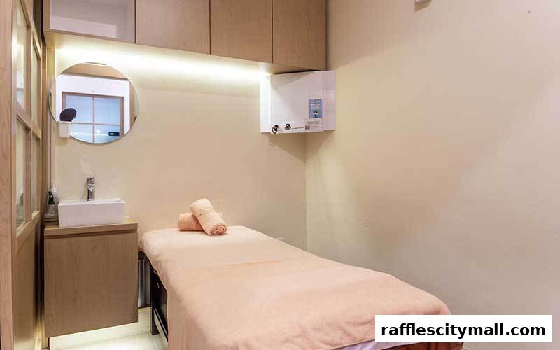 A clean and serene treatment room with a massage bed, sink, and mirror.