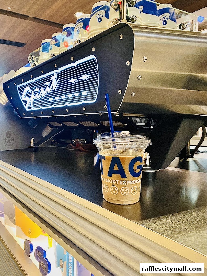 A close-up of an iced coffee with the TAG Espresso logo next to a professional espresso machine.