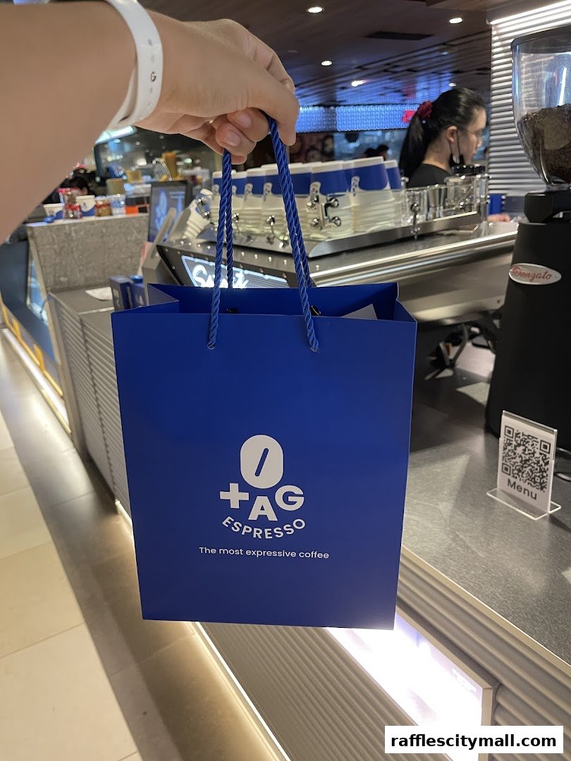 A hand holds a blue shopping bag from TAG Espresso with coffee shop interior in the background.