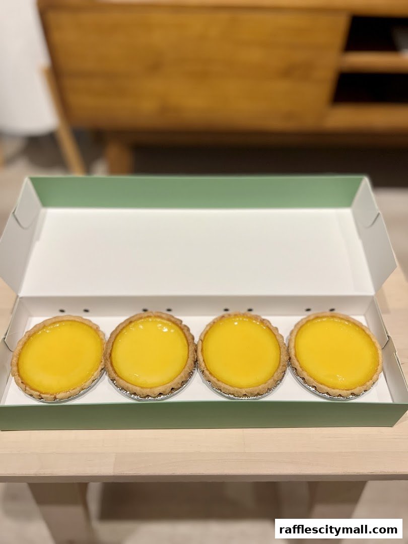 A box of four golden egg tarts with flaky crusts on a wooden surface.