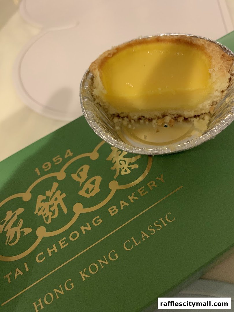 A close-up of a delicious egg tart from Tai Cheong Bakery on a green branded box.