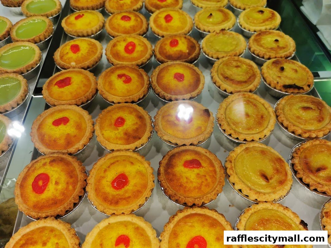 A display of freshly baked egg tarts and pandan tarts in a bakery.