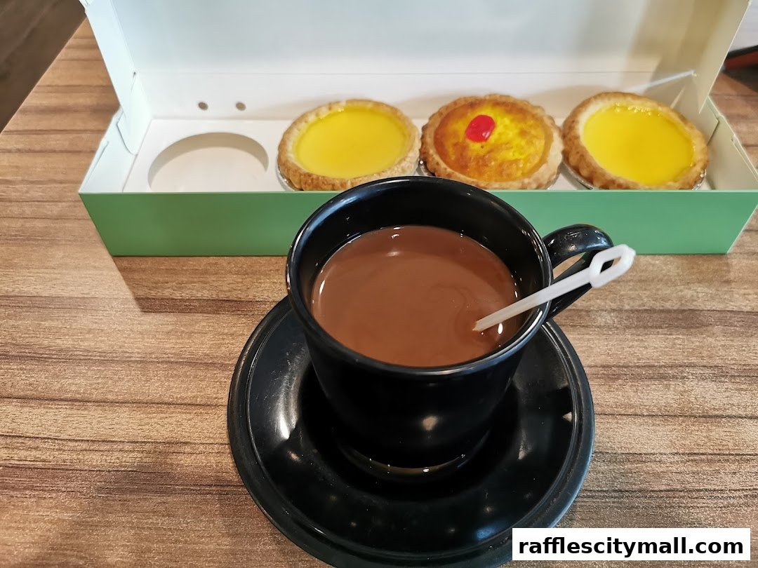 A black cup of coffee sits on a saucer next to a box of tarts.