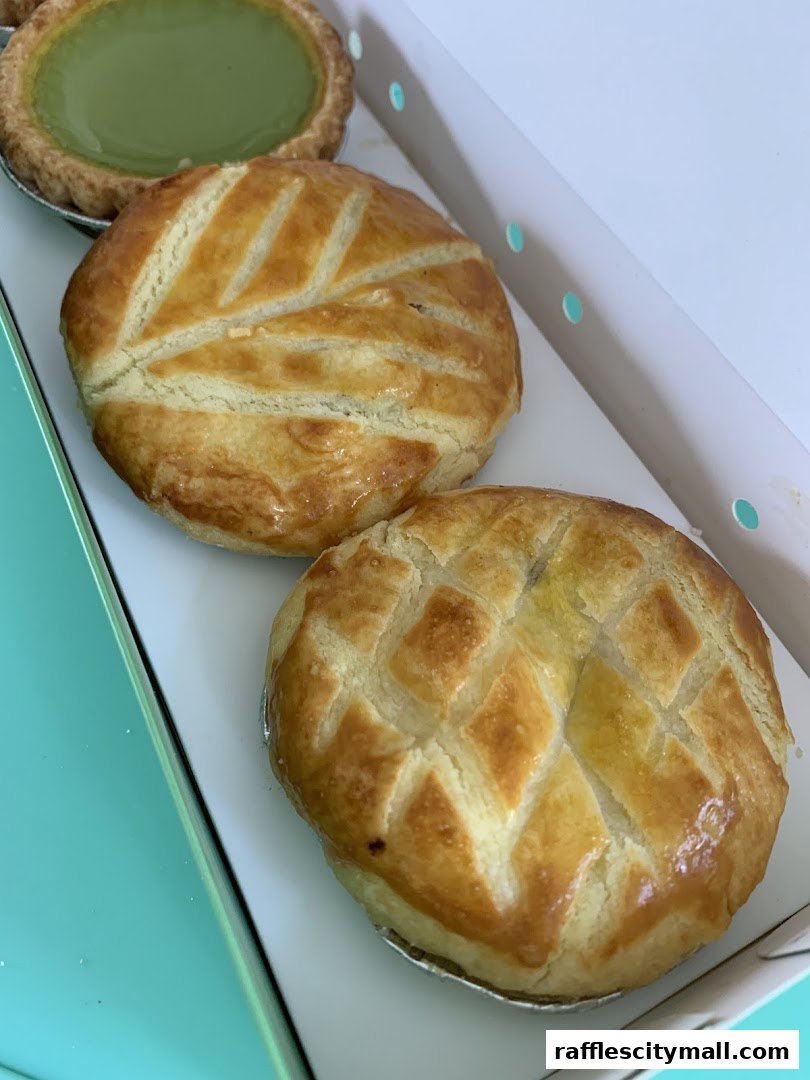 A close-up shot of freshly baked pastries and a green tart in a white box.