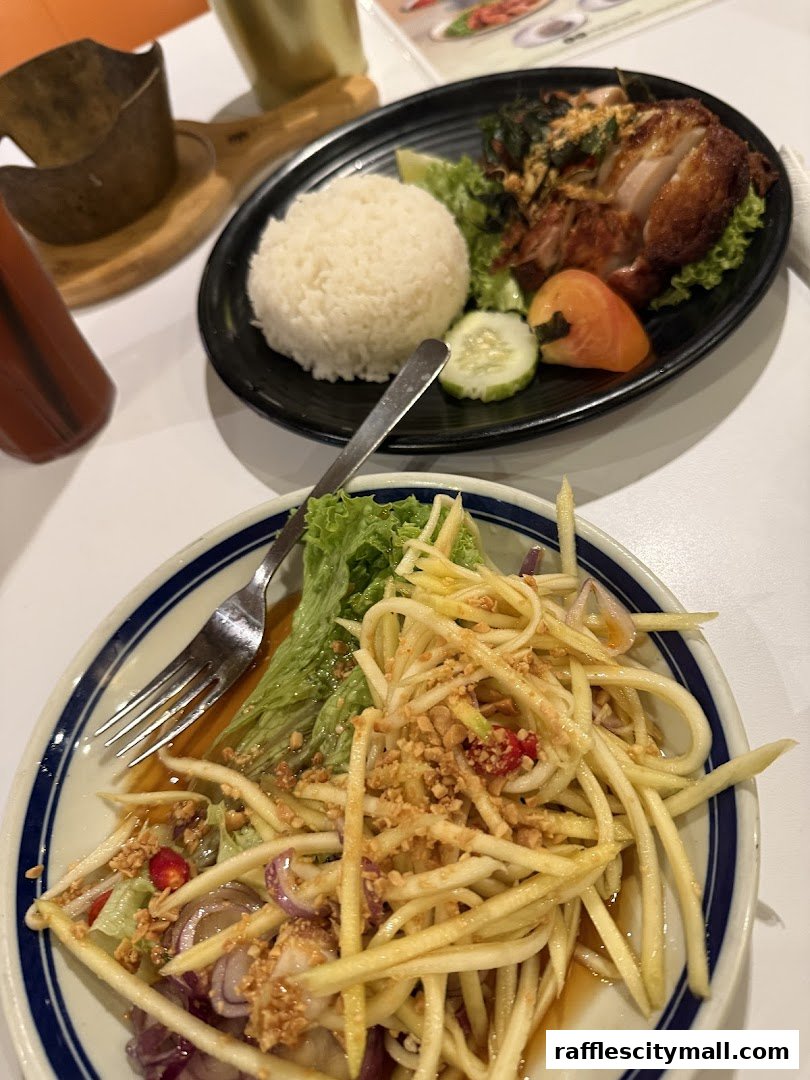 Two plates of Thai food, one with rice and fried chicken, the other with a mango salad.