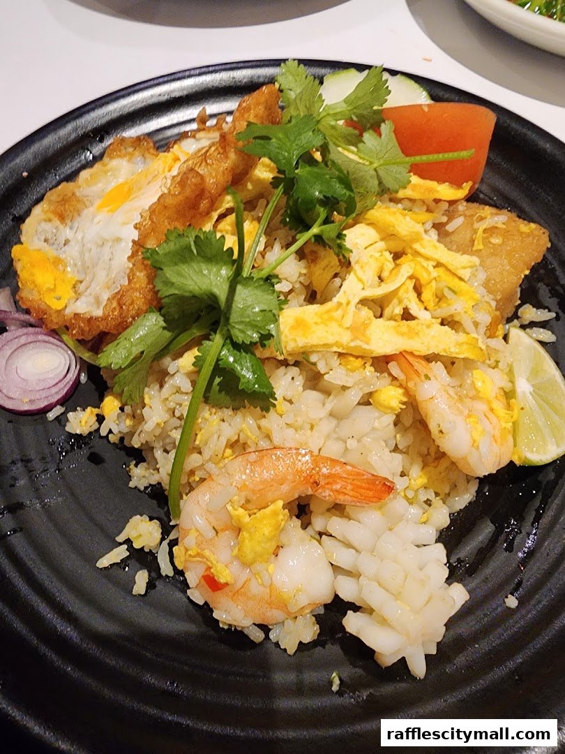 A plate of Thai fried rice with shrimp, calamari, a fried egg, and garnishes.