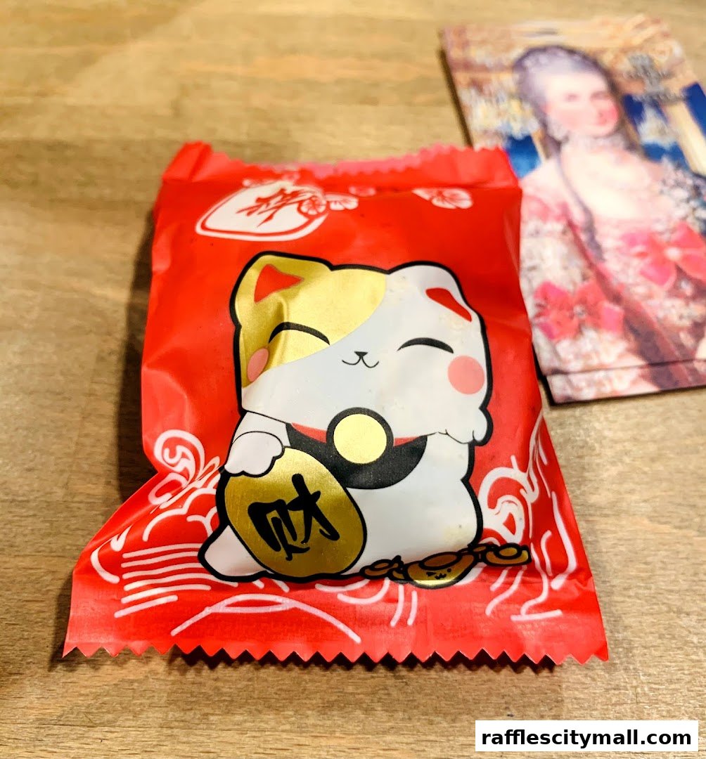 A red cookie wrapper with a lucky cat design and a historical portrait in the background.