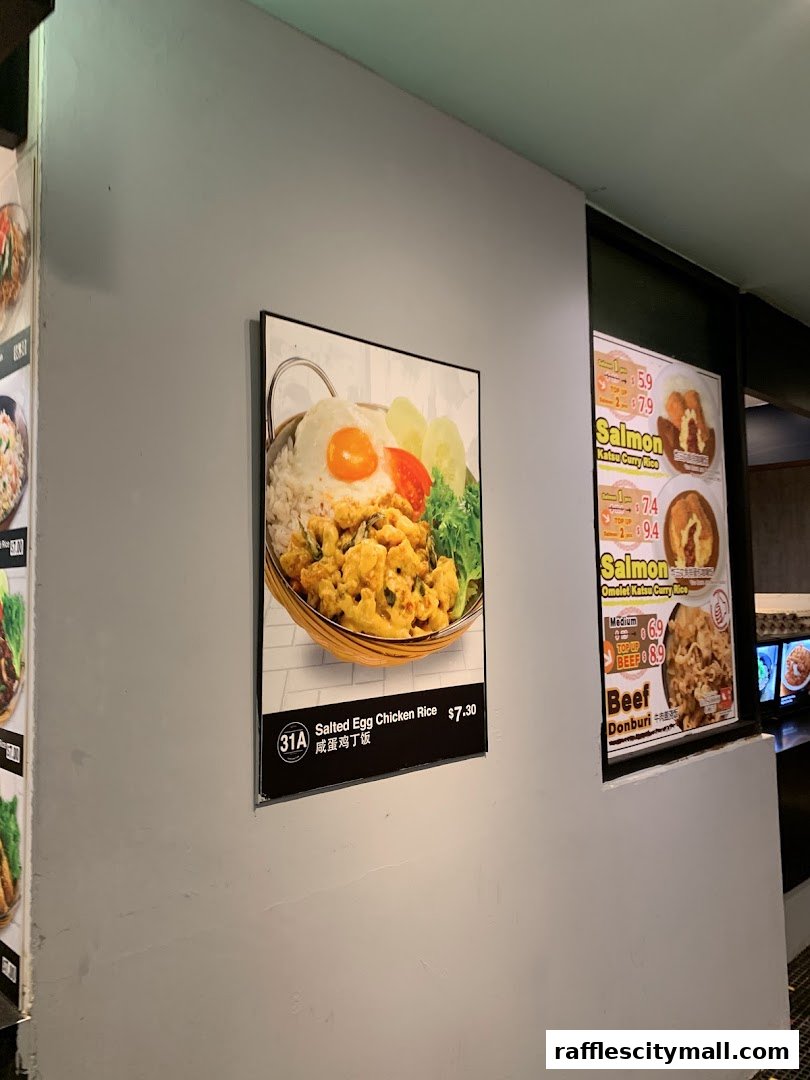 A poster of Salted Egg Chicken Rice is displayed on a grey wall next to other food advertisements.
