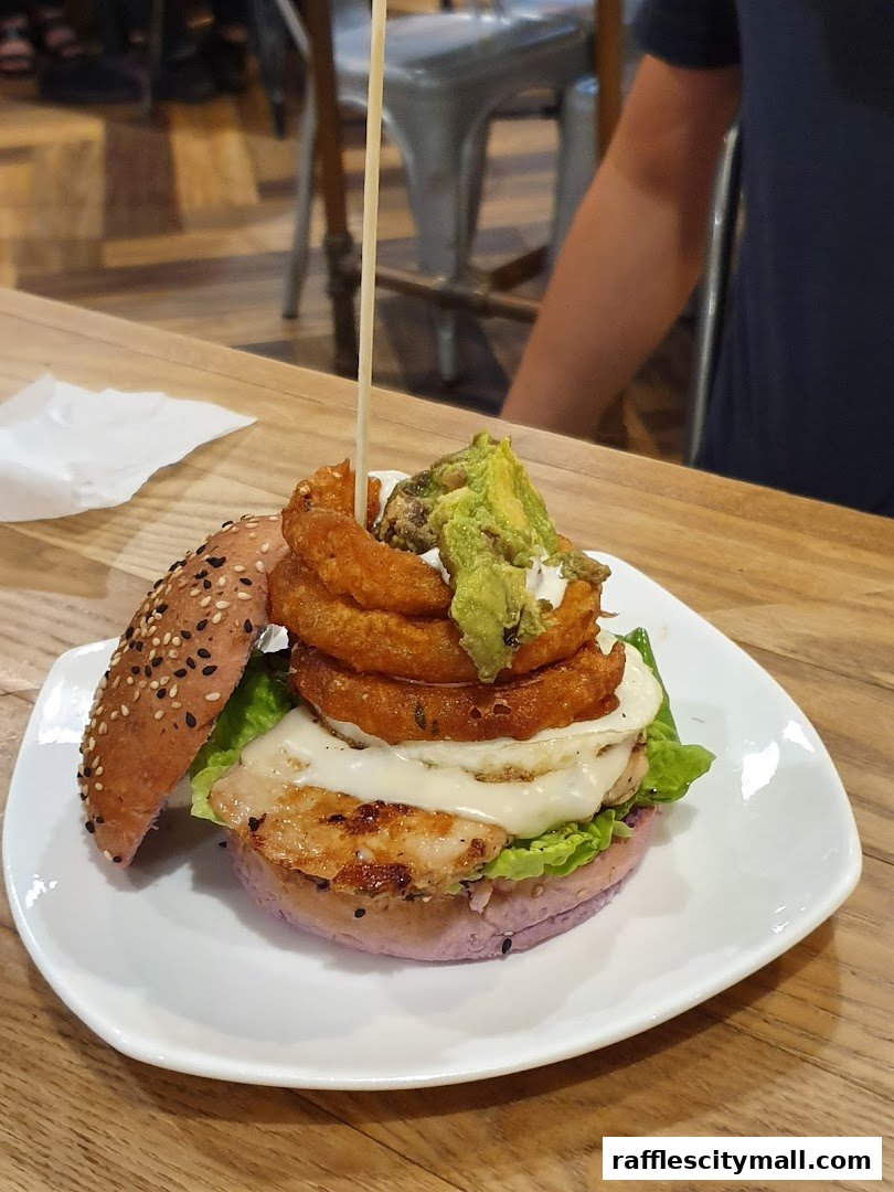 A gourmet burger with onion rings, avocado, and cheese on a purple bun.