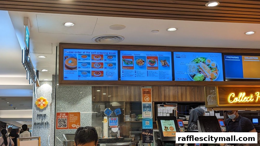 A digital menu board displays various soups, flatbreads, salads, and sandwiches at The Soup Spoon.