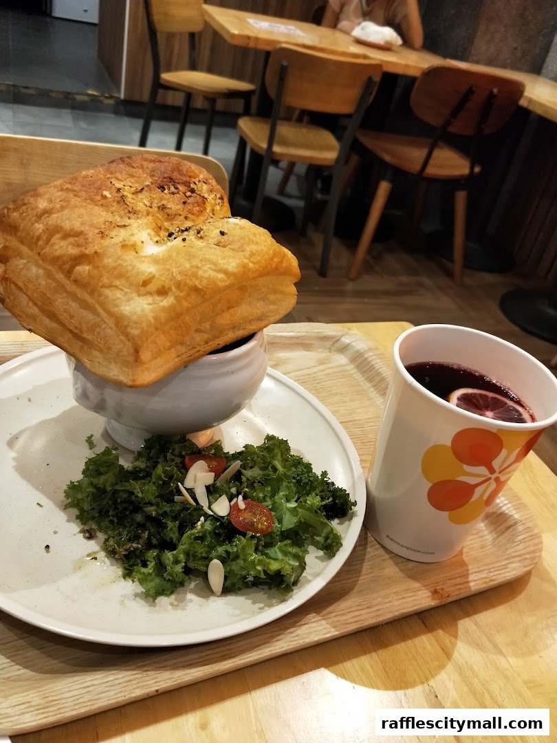 A hearty soup with a puff pastry lid, side salad, and a warm drink on a wooden tray.
